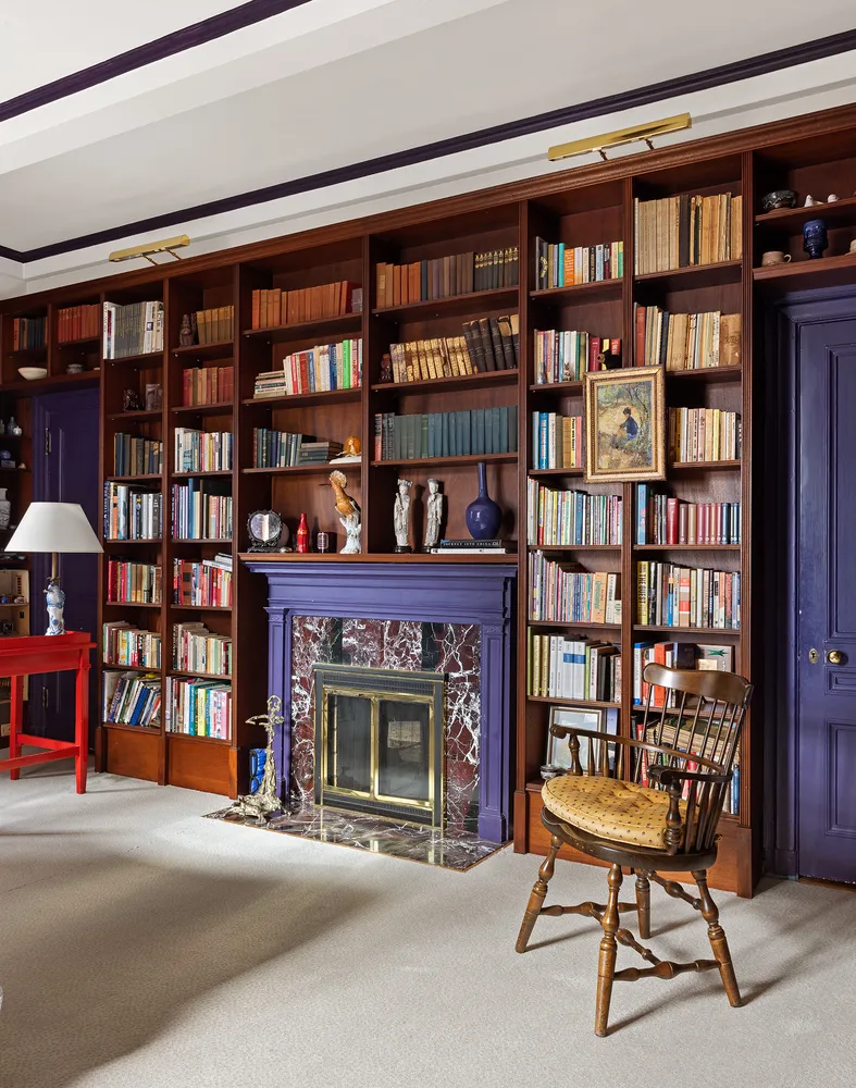 a living room with bookshelf a table and a fireplace