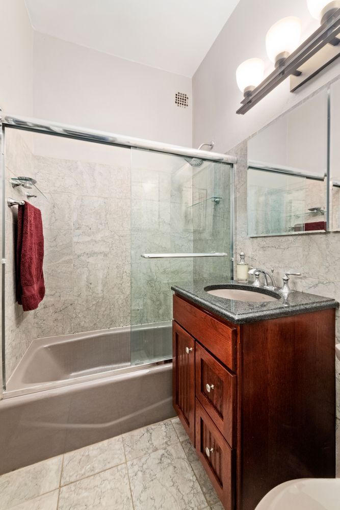 345 East 54th Street Manhattan, NY 10022 - Photo 7 of 10 a bathroom with a granite countertop sink a mirror a bathtub and shower