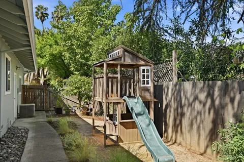 a view of a wooden house with large trees and wooden fence