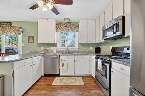 a kitchen with stainless steel appliances granite countertop a refrigerator a stove a sink dishwasher and a dining table with wooden floor