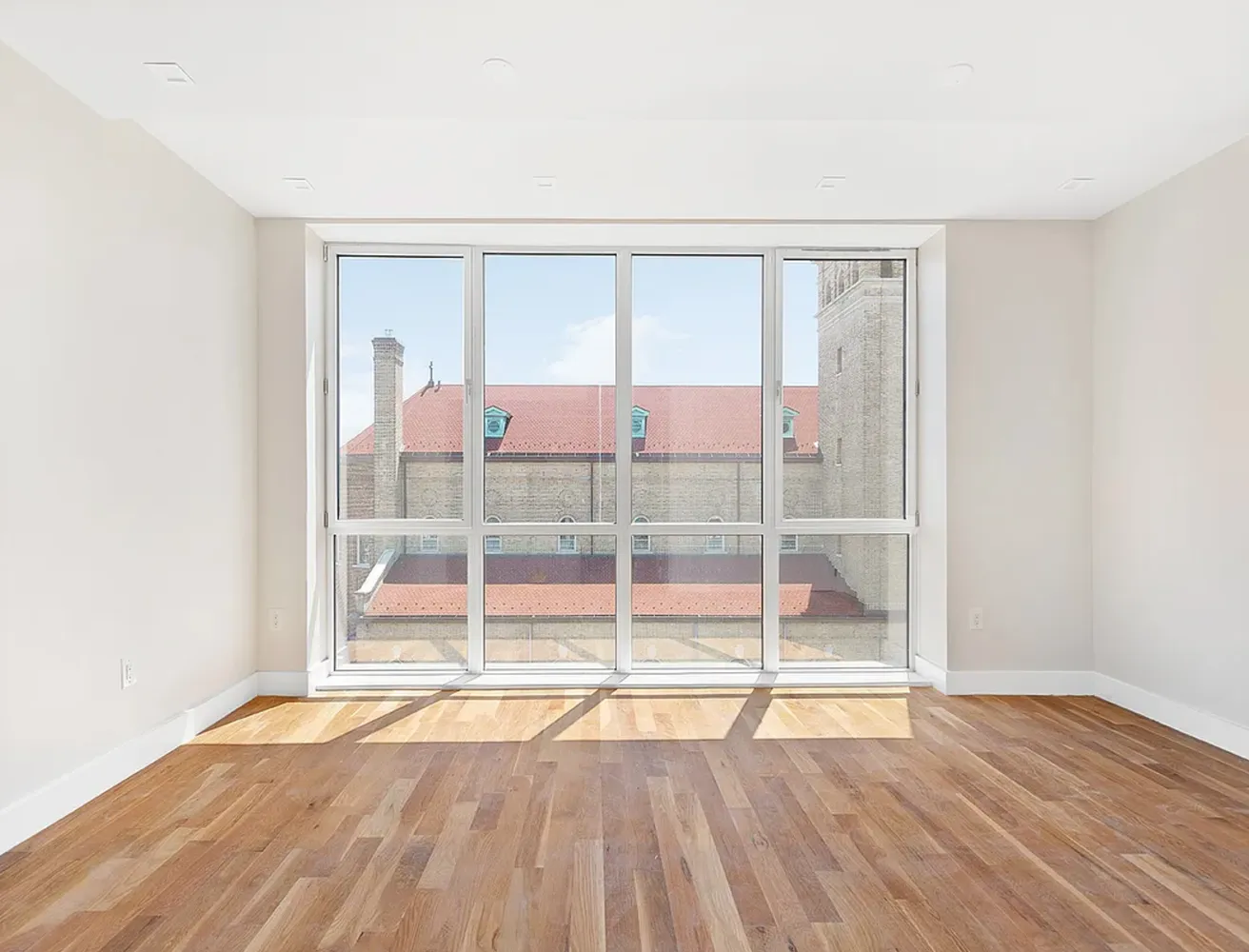a view of an empty room with wooden floor and a window