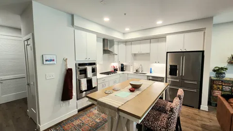 a living room with stainless steel appliances furniture a rug and a kitchen view