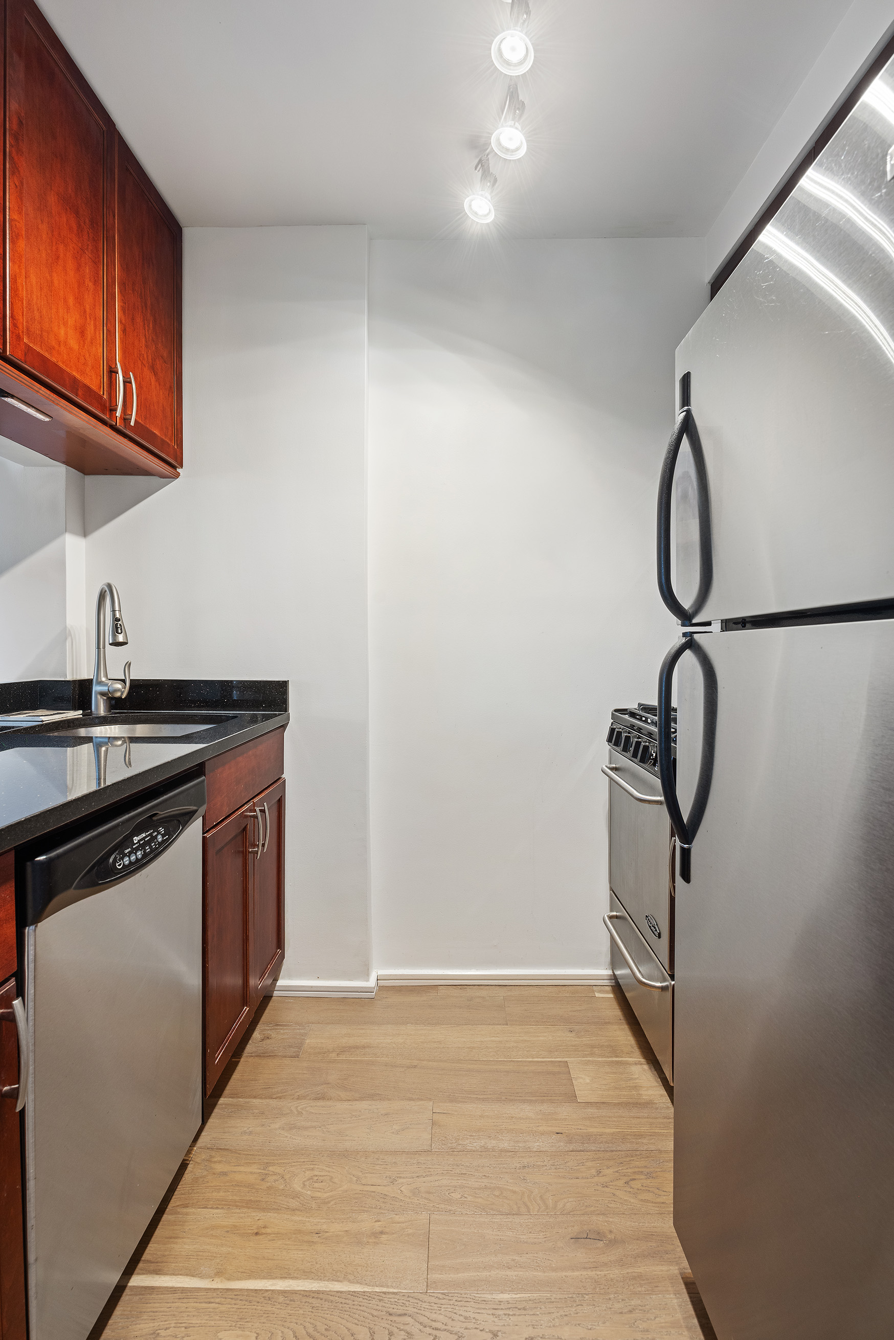 415 East 85th Street, Unit 7J Manhattan, NY 10028 - Photo 4 of 9 a kitchen with stainless steel appliances granite countertop a sink stove and a wooden floor