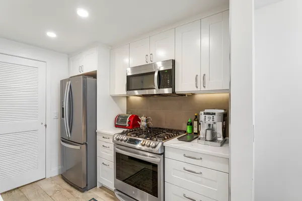 a kitchen with stainless steel appliances a stove a sink a microwave a dining table and chairs with wooden floor