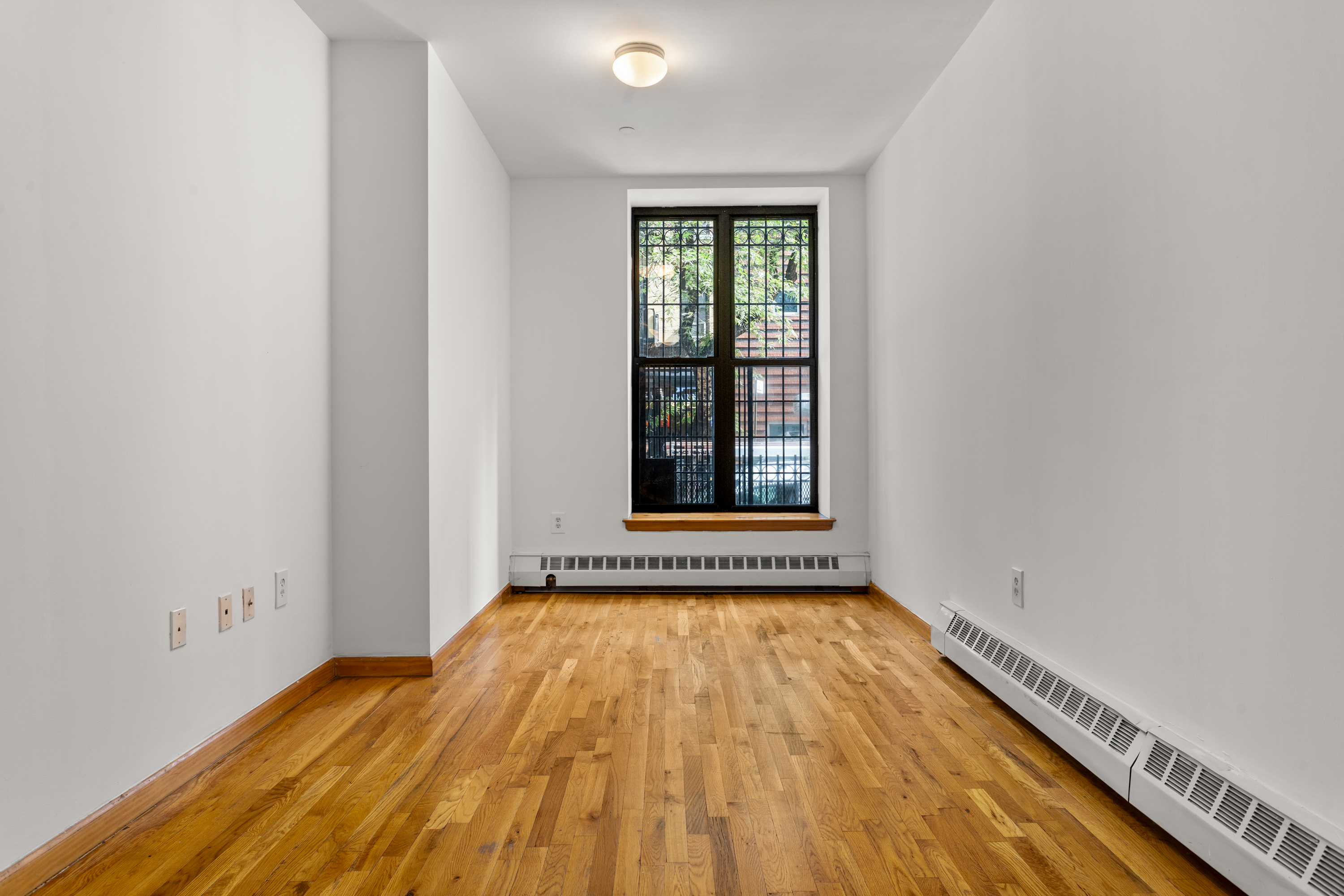 316 West 47th Street, Unit 1FE Manhattan, NY 10036 - Photo 3 of 9 a view of an empty room with exposed radiator and wooden floor