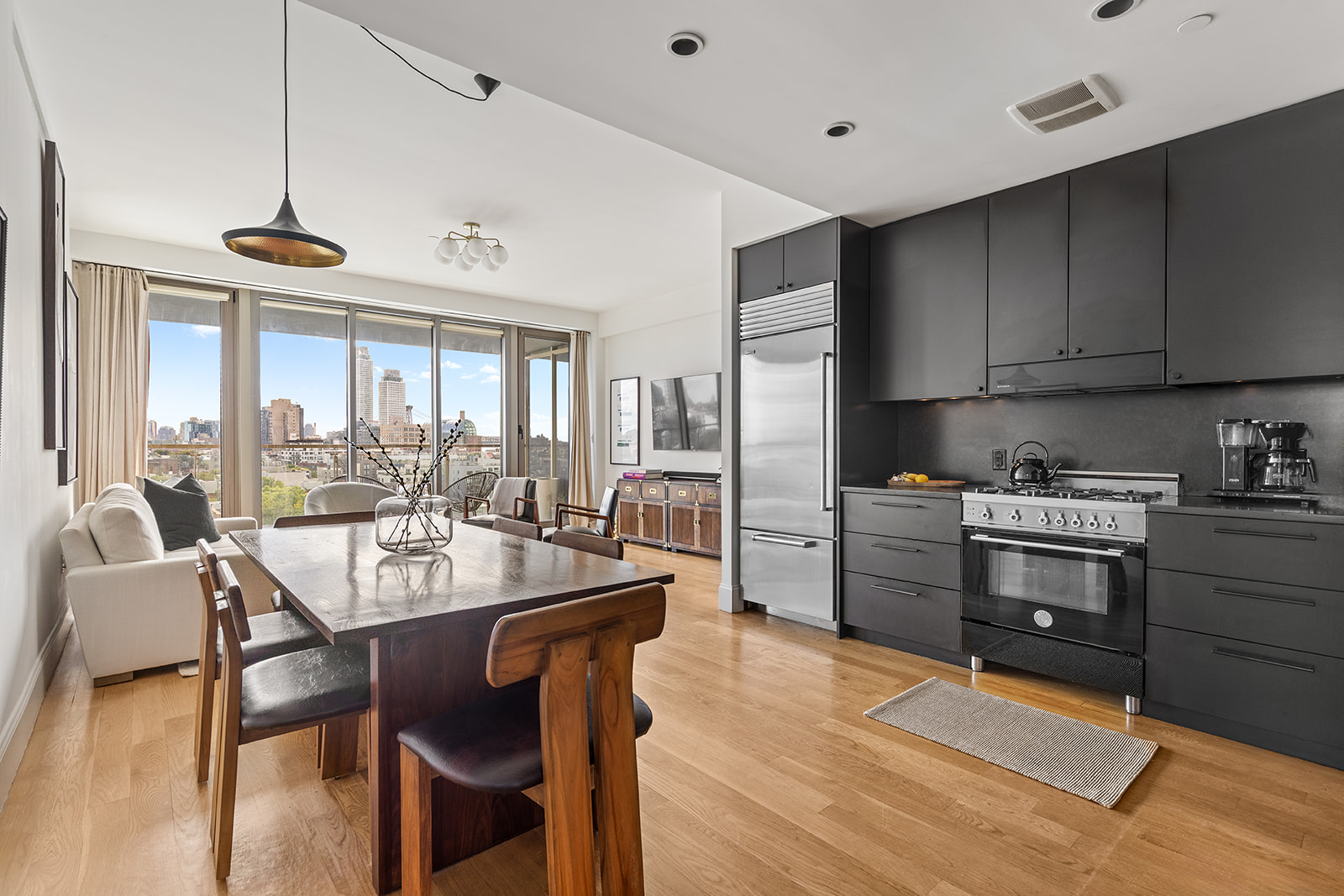 144 North 8th Street, Unit 8C Brooklyn, NY 11249 - Photo 2 of 13 a kitchen with stainless steel appliances kitchen island granite countertop a table chairs and a wooden cabinets