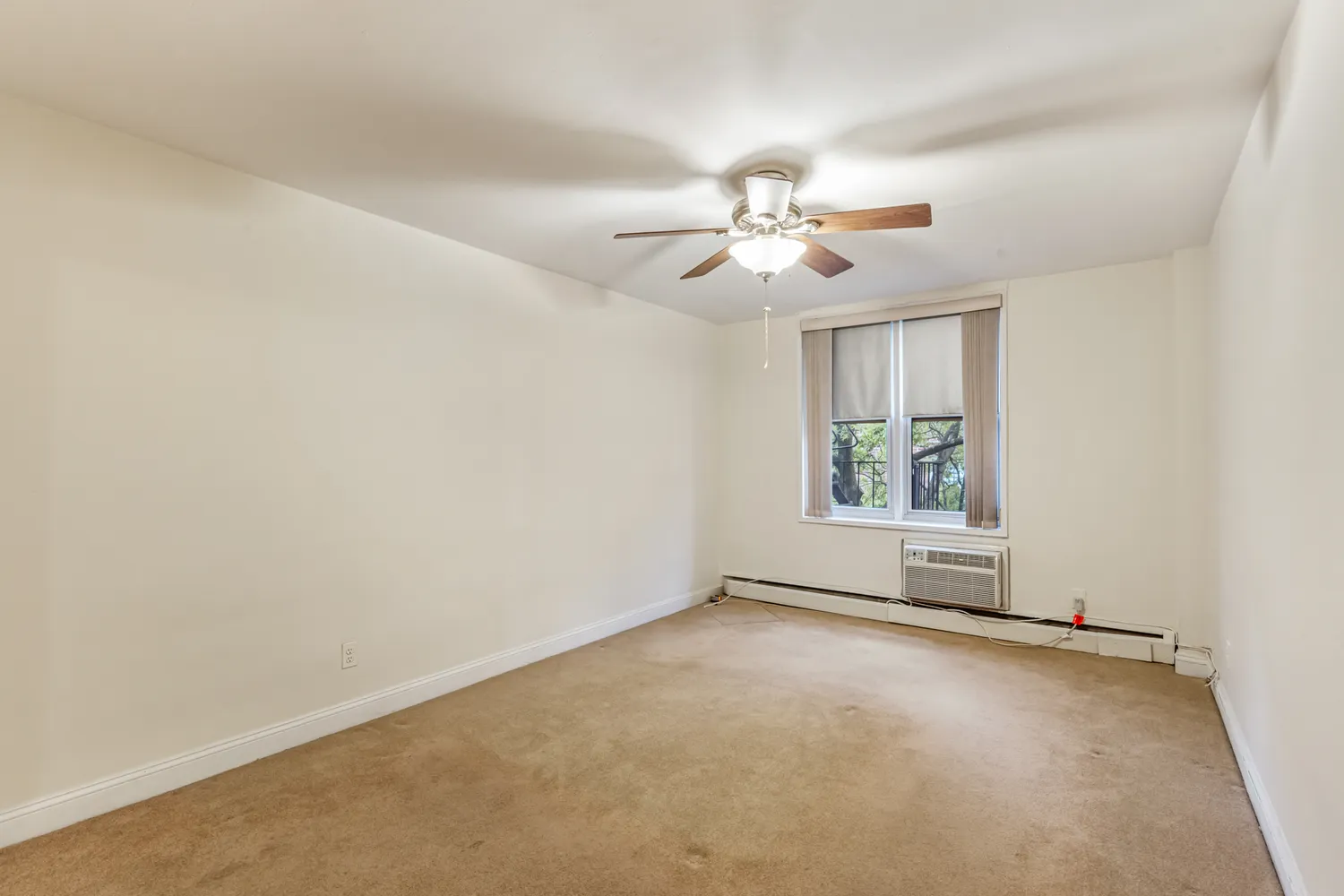 an empty room with chandelier fan and kitchen view