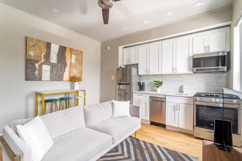 a living room with stainless steel appliances furniture a flat screen tv and a kitchen view