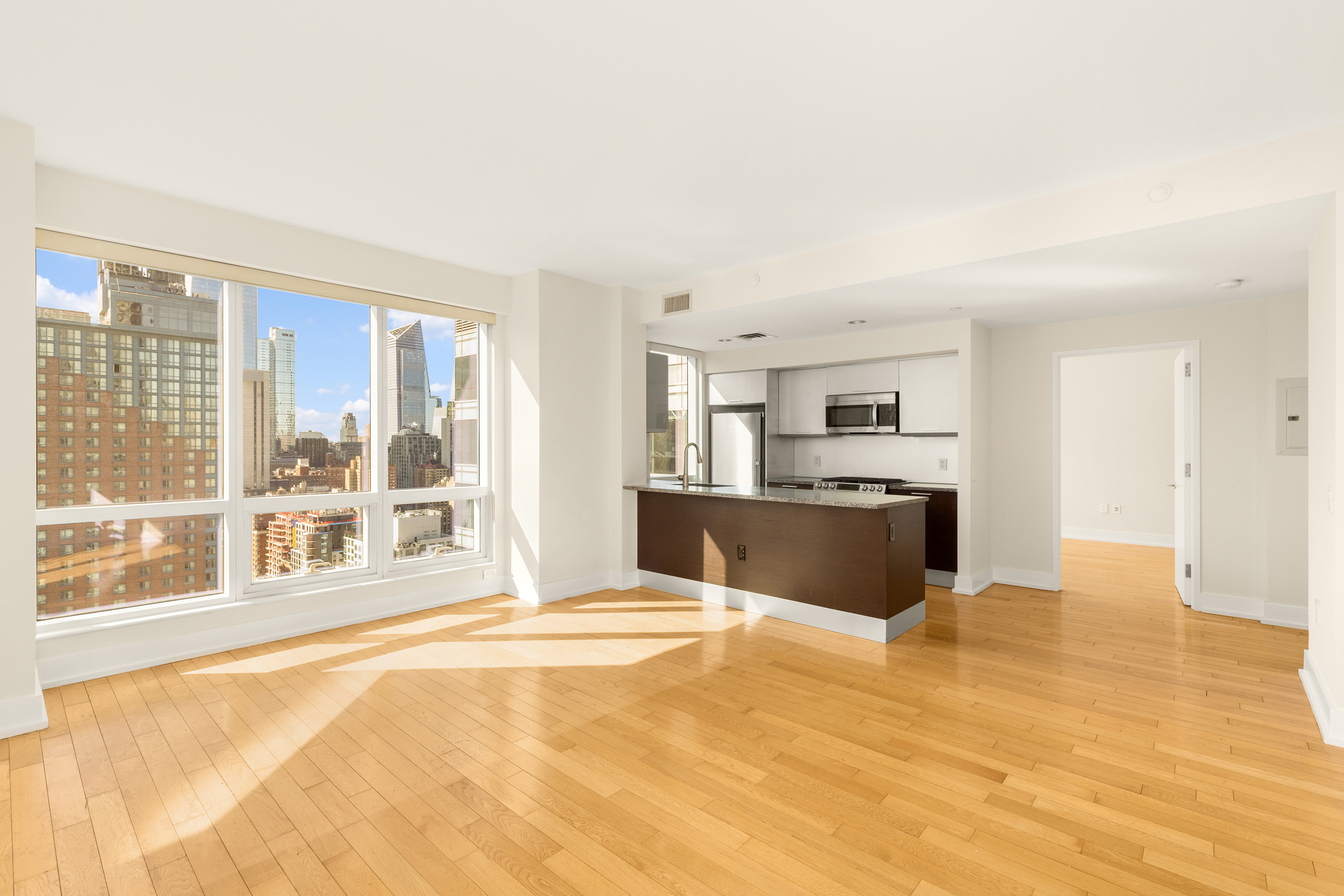 350 West 42nd Street, Unit 26G Manhattan, NY 10036 - Photo 4 of 11 a large white kitchen with kitchen island a sink wooden floor and a large window