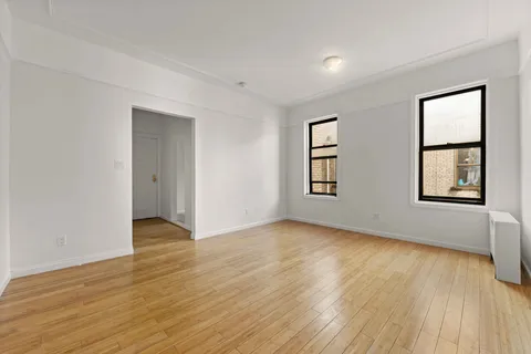 a view of an empty room with window and wooden floor