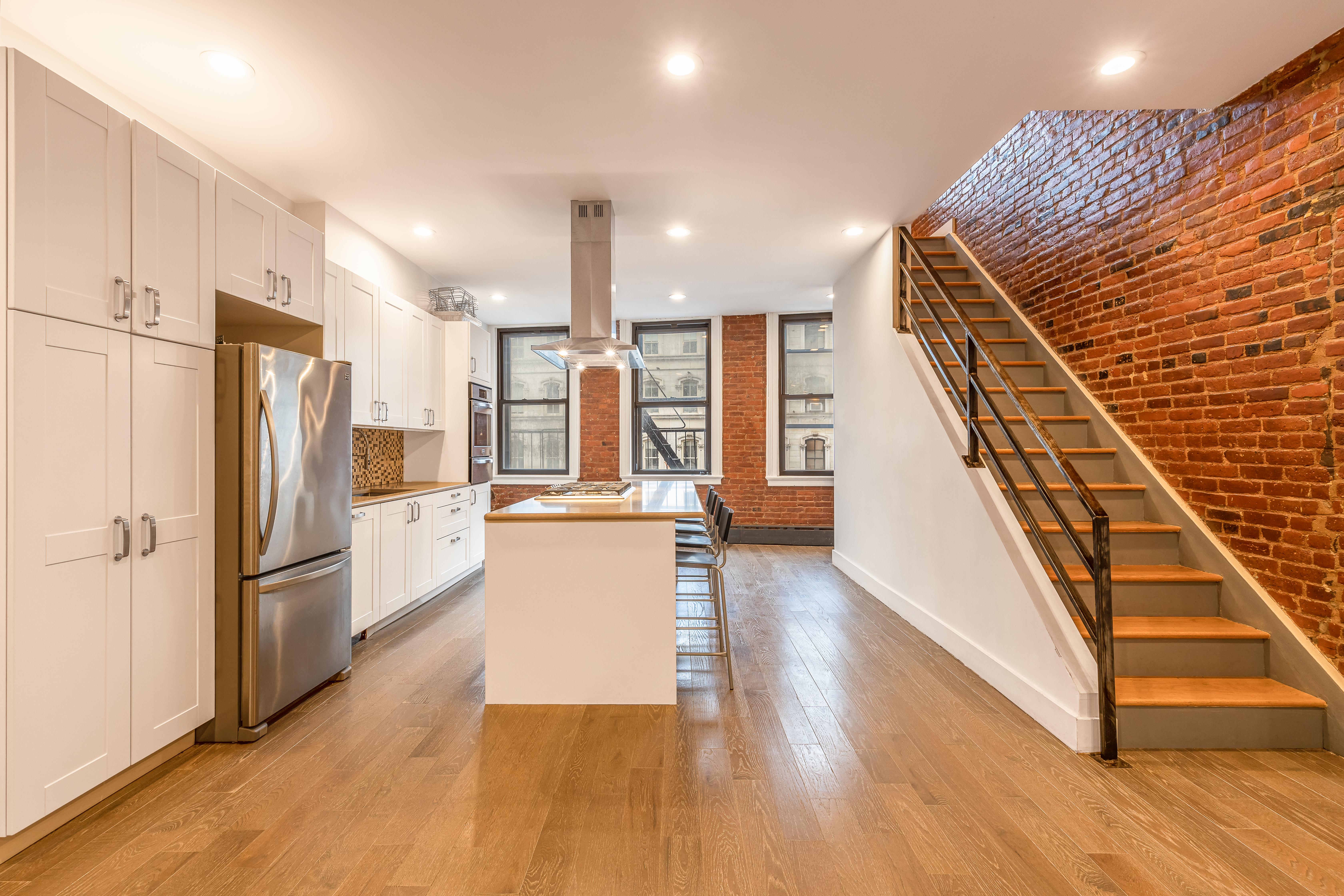 61 Lispenard Street, Unit 4 Manhattan, NY 10013 - Photo 2 of 8 a kitchen with stainless steel appliances kitchen island wooden floors granite counter tops and white cabinets