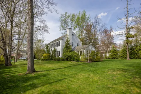 a view of a white house with a big yard and potted plants and large trees