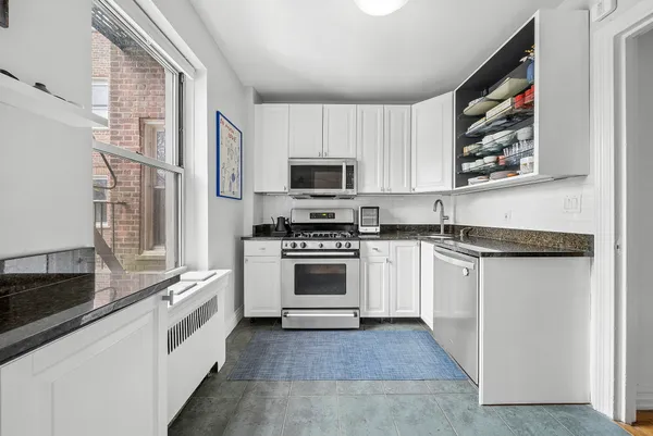 a white kitchen with granite countertop a stove and a sink