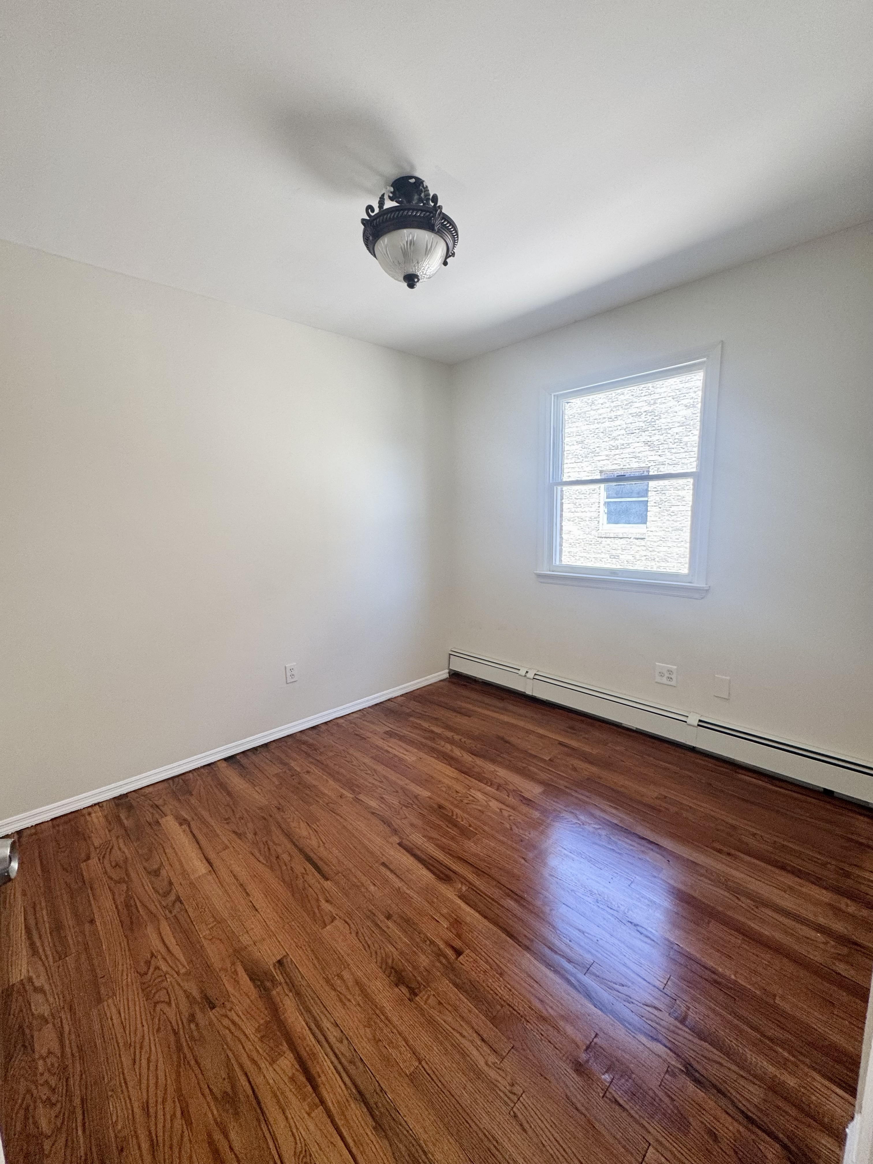 156-17 76th Street, Unit 1 Queens, NY 11414 - Photo 8 of 12 an empty room with wooden floor and windows