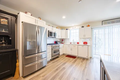 a kitchen with granite countertop a refrigerator oven a sink dishwasher and white cabinets with wooden floor