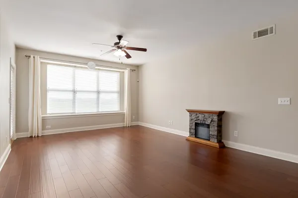 an empty room with wooden floor chandelier fan and windows