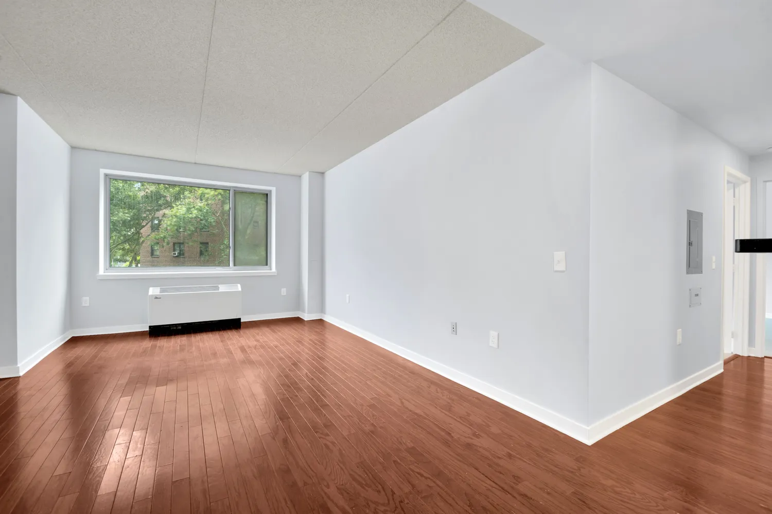 a view of an empty room with wooden floor and a window