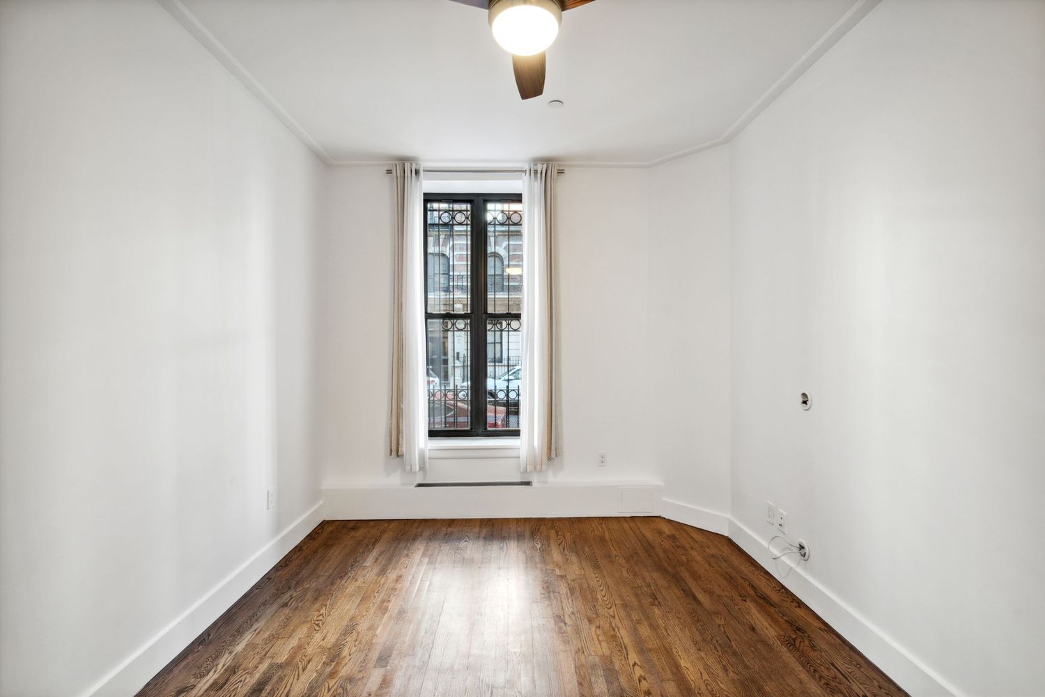 an empty room with wooden floor chandelier fan and windows