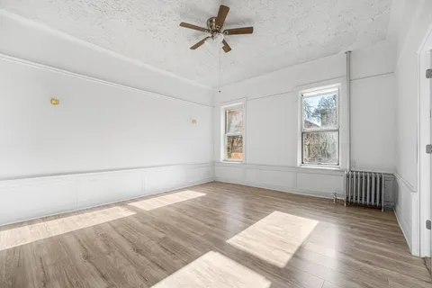 an empty room with wooden floor fan and windows