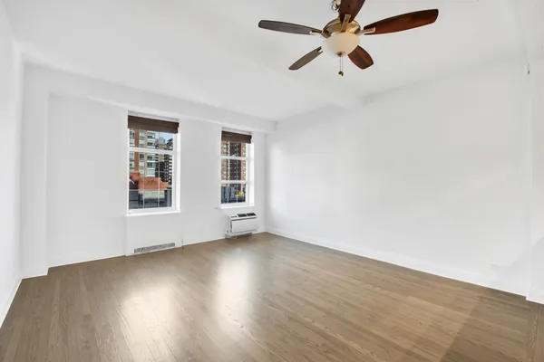 an empty room with wooden floor chandelier fan and windows