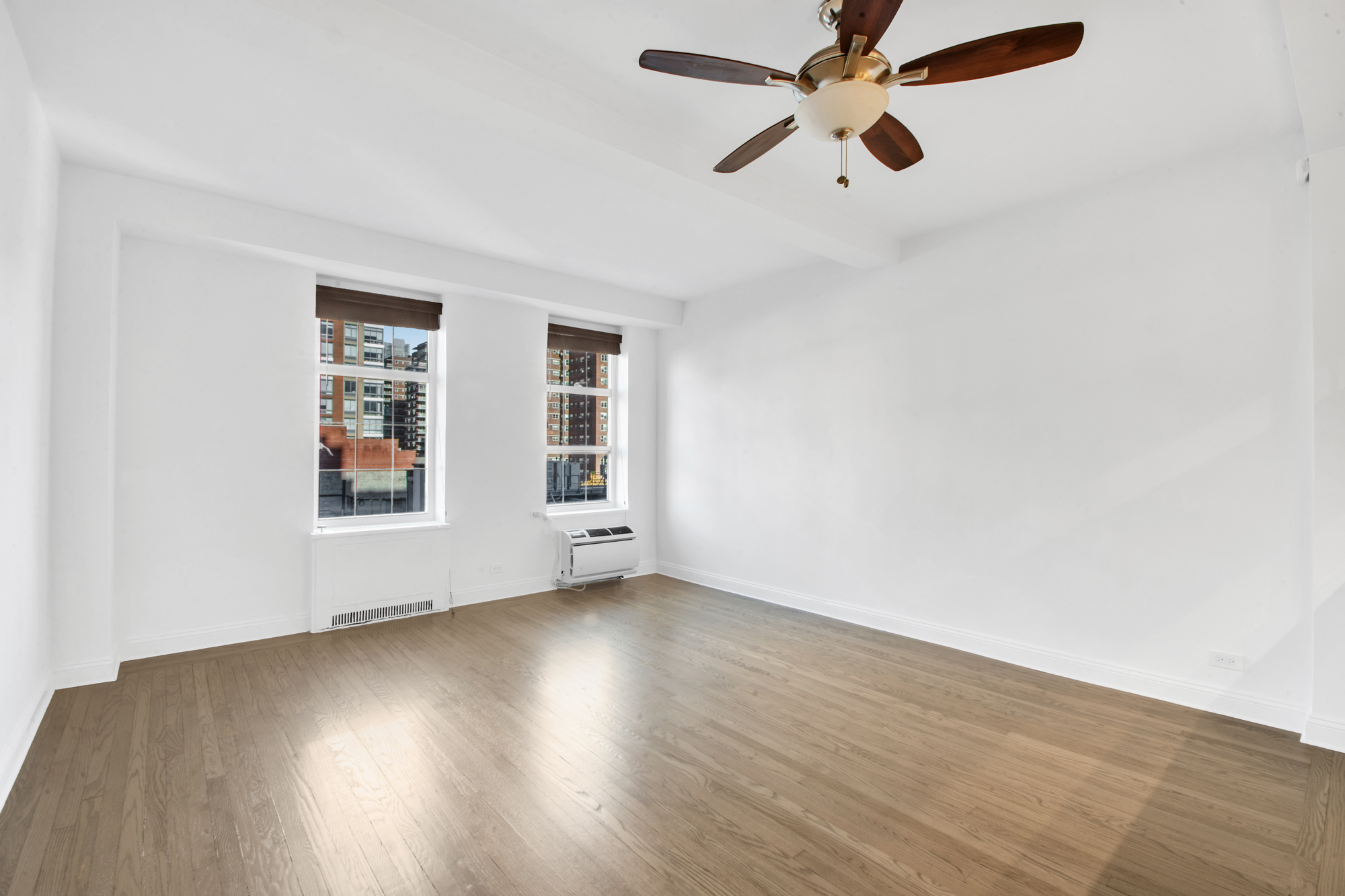 410 West 24th Street, Unit 9K Manhattan, NY 10011 - Photo 4 of 14 an empty room with wooden floor chandelier fan and windows