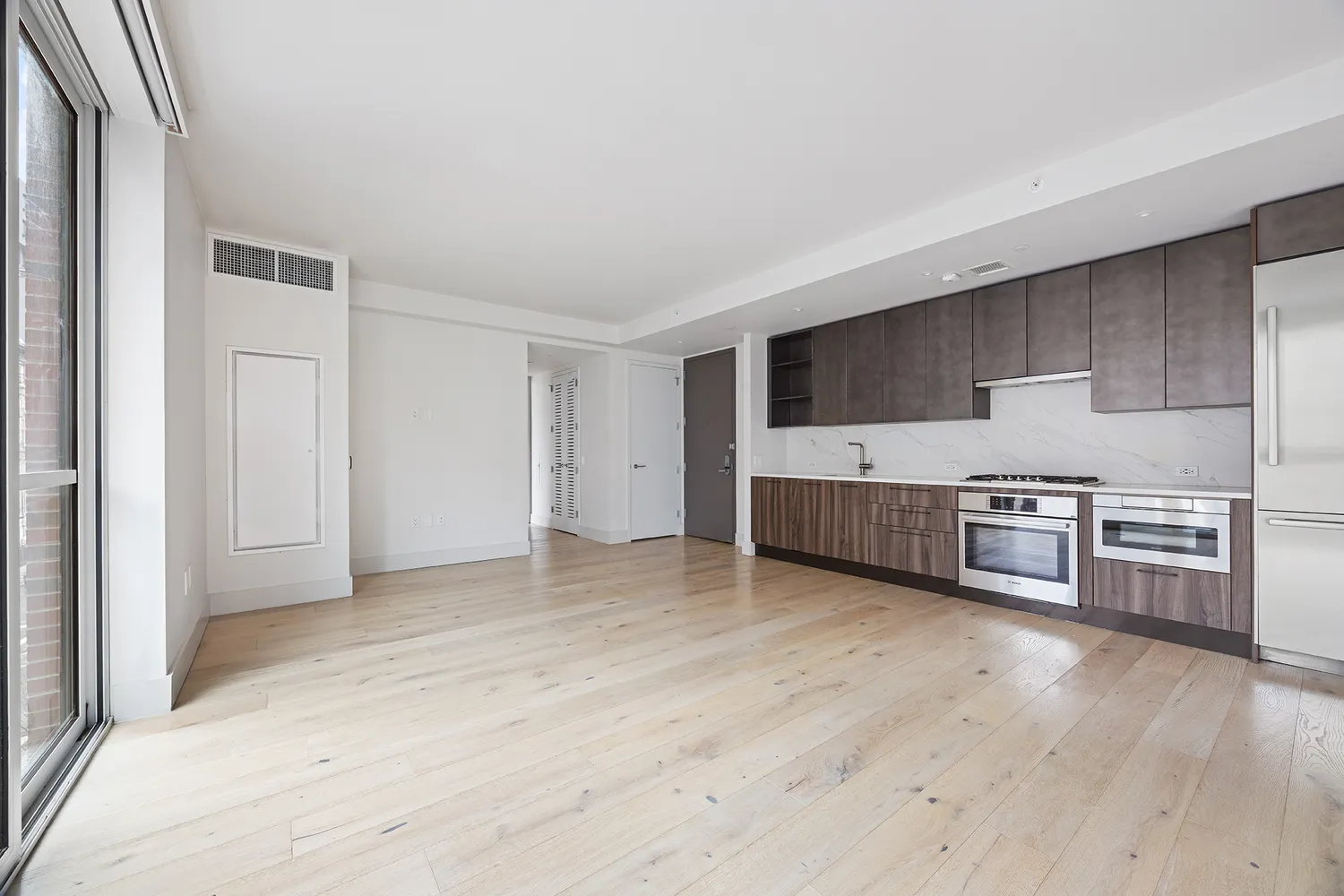 a view of an empty room with a window and a kitchen