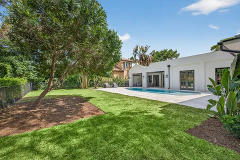 a white house with a big yard plants and large trees