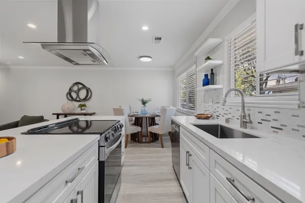 a kitchen with a sink dishwasher a stove and white cabinets with wooden floor