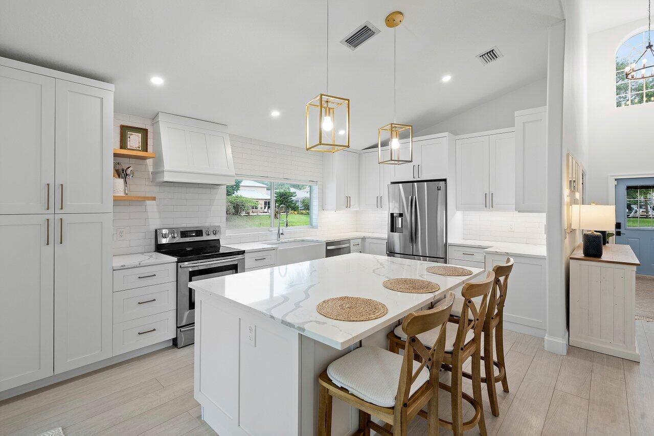 1182 Canoe Point Delray Beach, FL 33444 - Photo 11 of 46 a kitchen with stainless steel appliances granite countertop a stove a refrigerator a white table and chairs with wooden floor