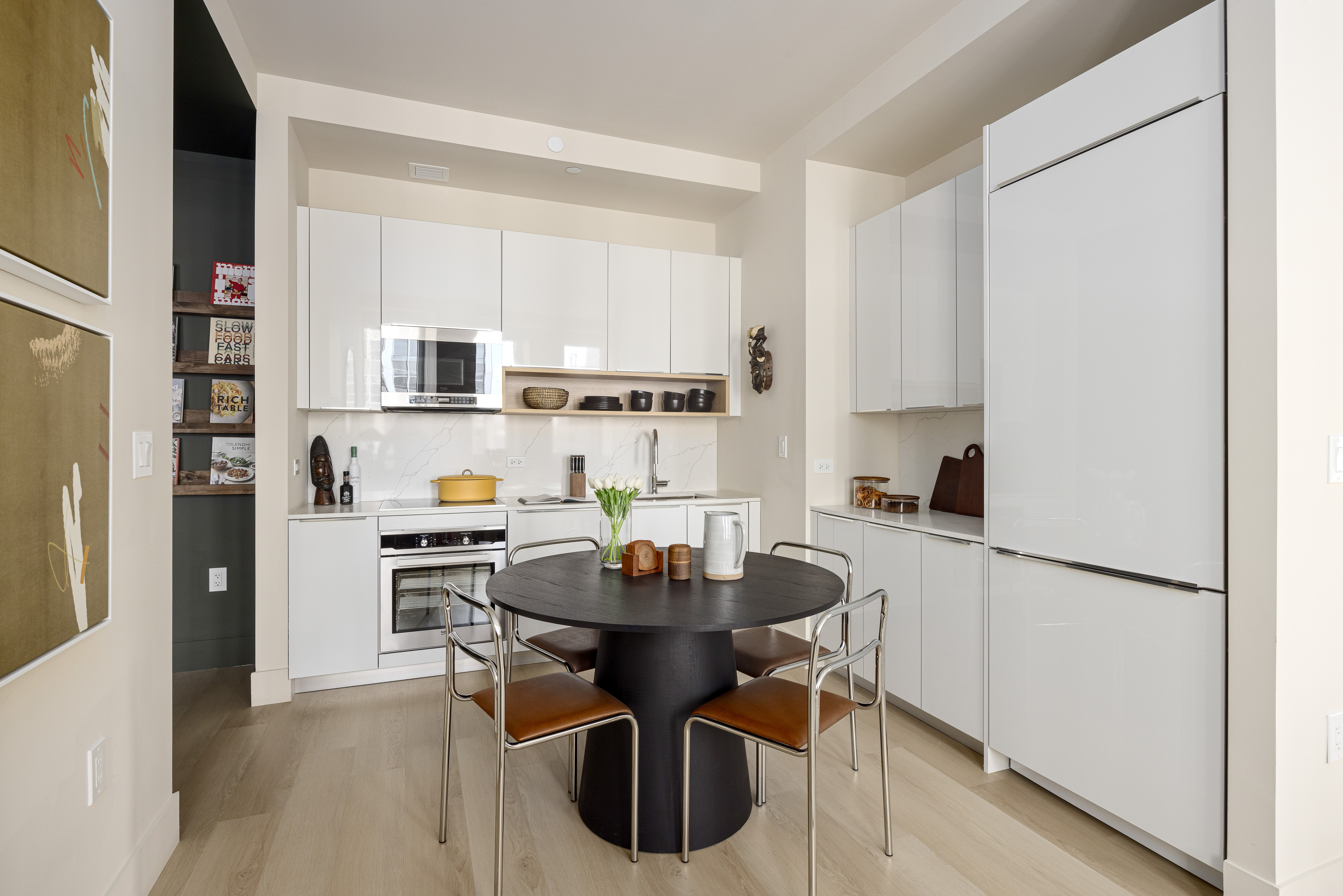 a living room with stainless steel appliances a dining table wooden floor and a refrigerator