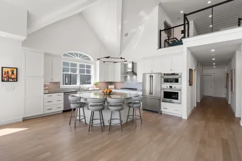 a kitchen with stainless steel appliances kitchen island granite countertop a stove a refrigerator a dining table and chairs with wooden floor