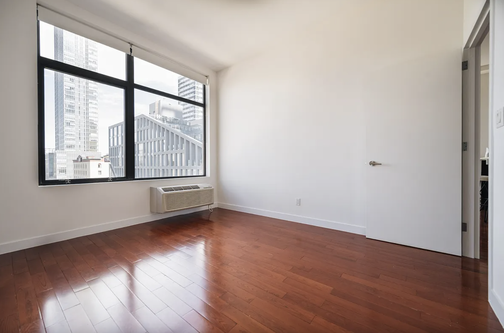 42-37 27th Street, Unit 8B Queens, NY 11101 - Photo 3 of 11 an empty room with wooden floor and windows