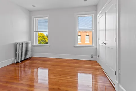 a view of an empty room with window and wooden floor