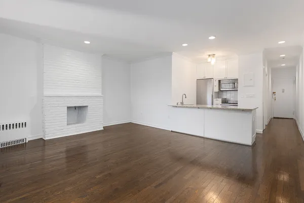 an empty room with wooden floor and kitchen view
