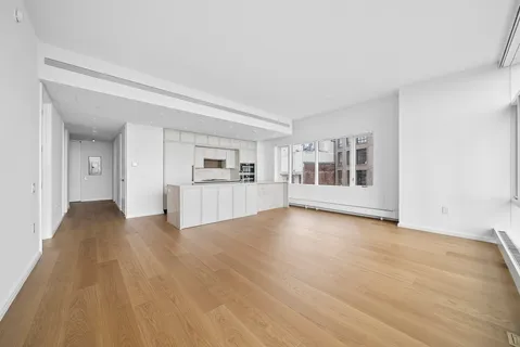 a view of empty room with wooden floor and kitchen view