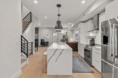 a large kitchen with stainless steel appliances kitchen island granite countertop a refrigerator a stove a sink dishwasher and white cabinets with wooden floor