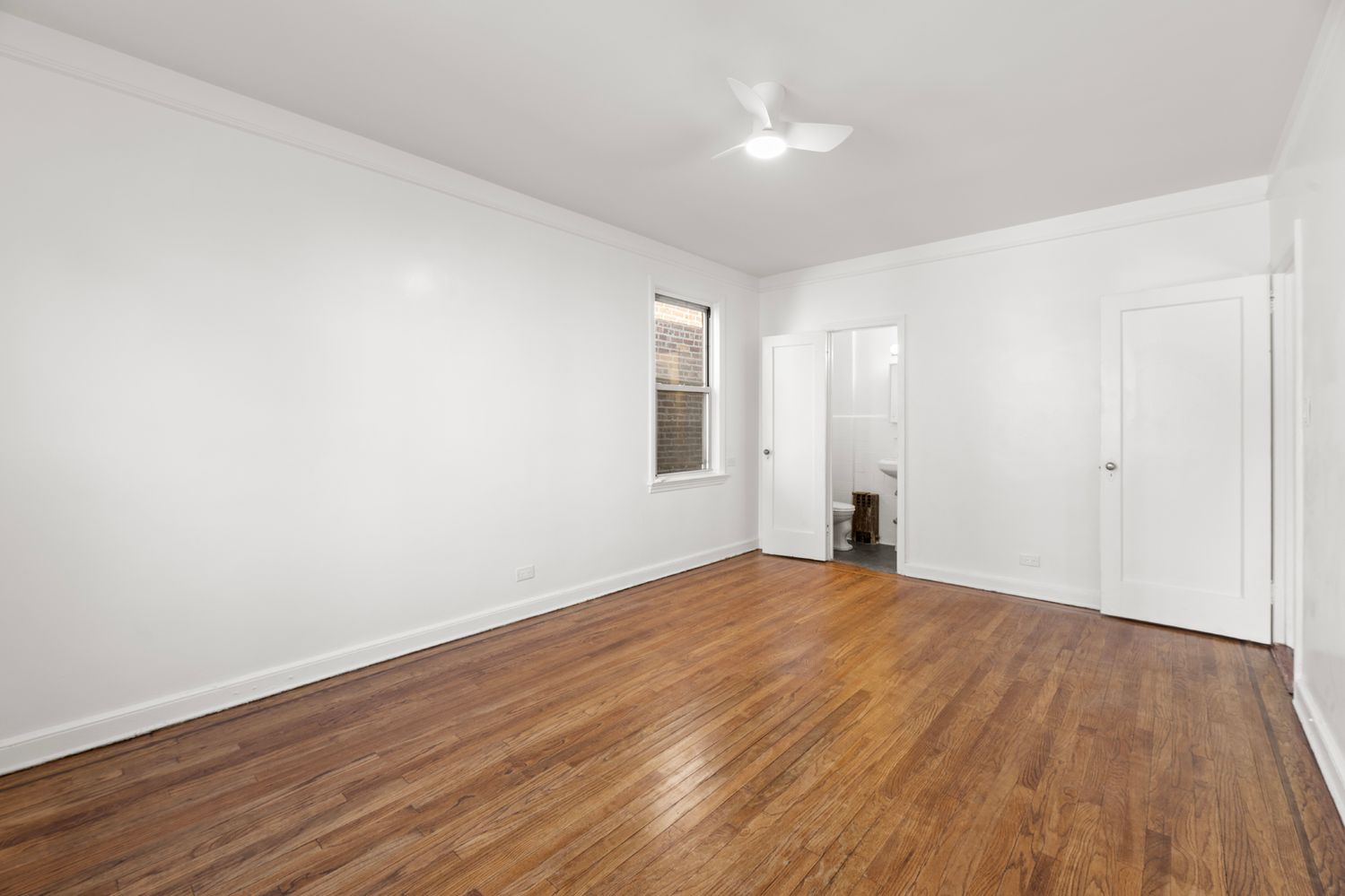 a view of empty room with wooden floor and fan