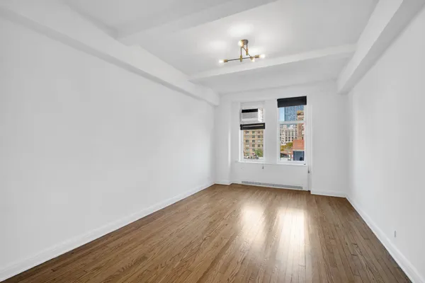 an empty room with wooden floor chandelier and windows