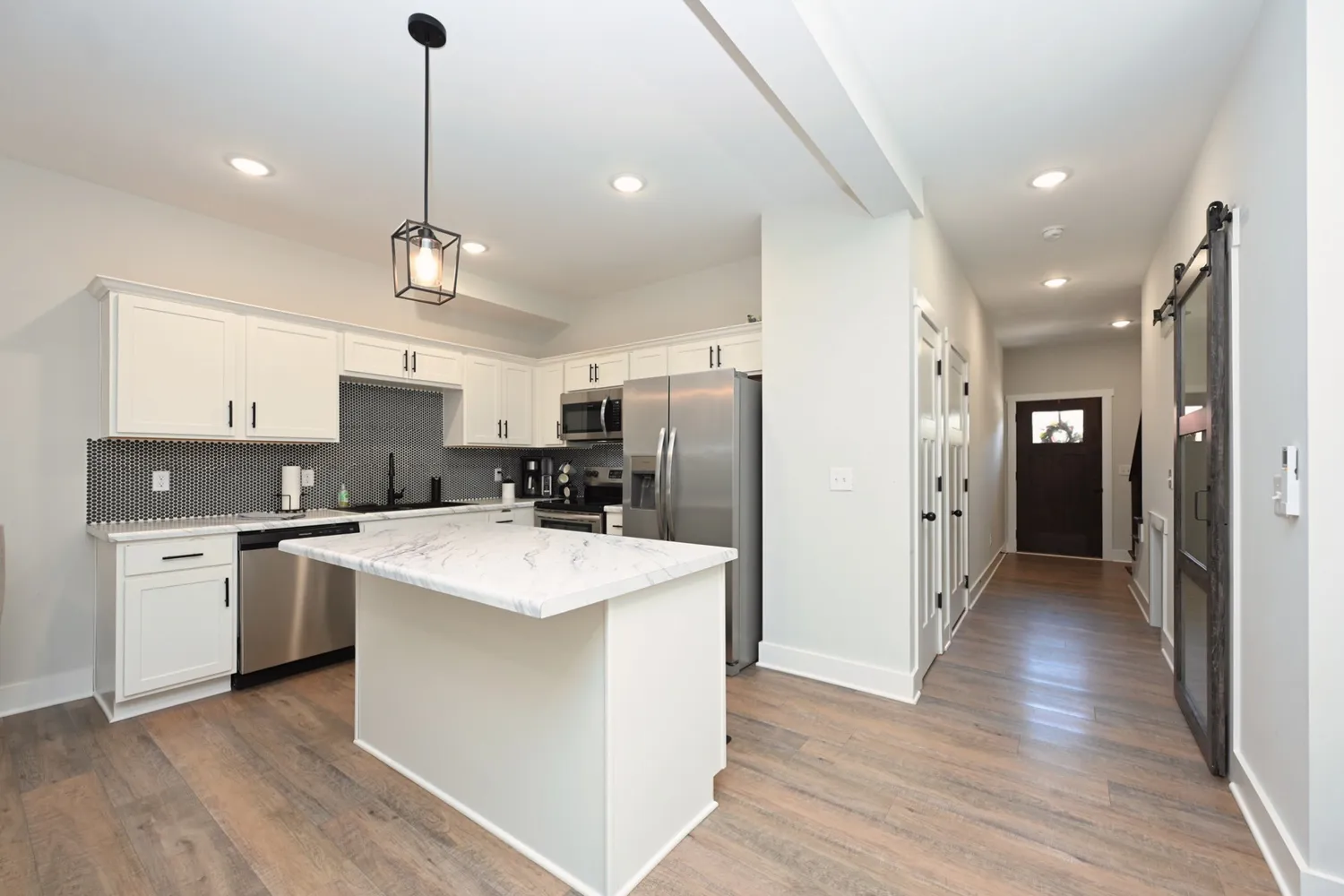 a kitchen with stainless steel appliances kitchen island a refrigerator a sink dishwasher a stove and white cabinets with wooden floor