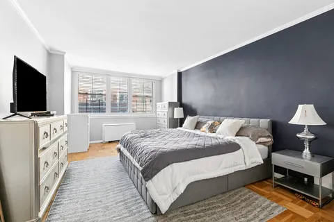 a spacious bedroom with a bed and a flat tv screen on dresser