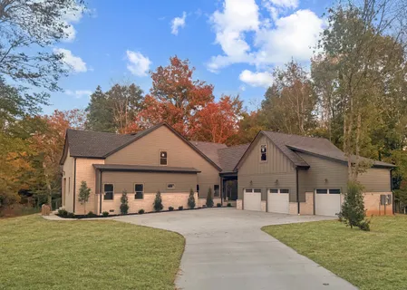 a view of a white house next to a yard with big trees and plants