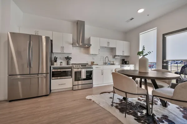 a kitchen with stainless steel appliances a refrigerator a stove a sink dishwasher and a dining table with wooden floor