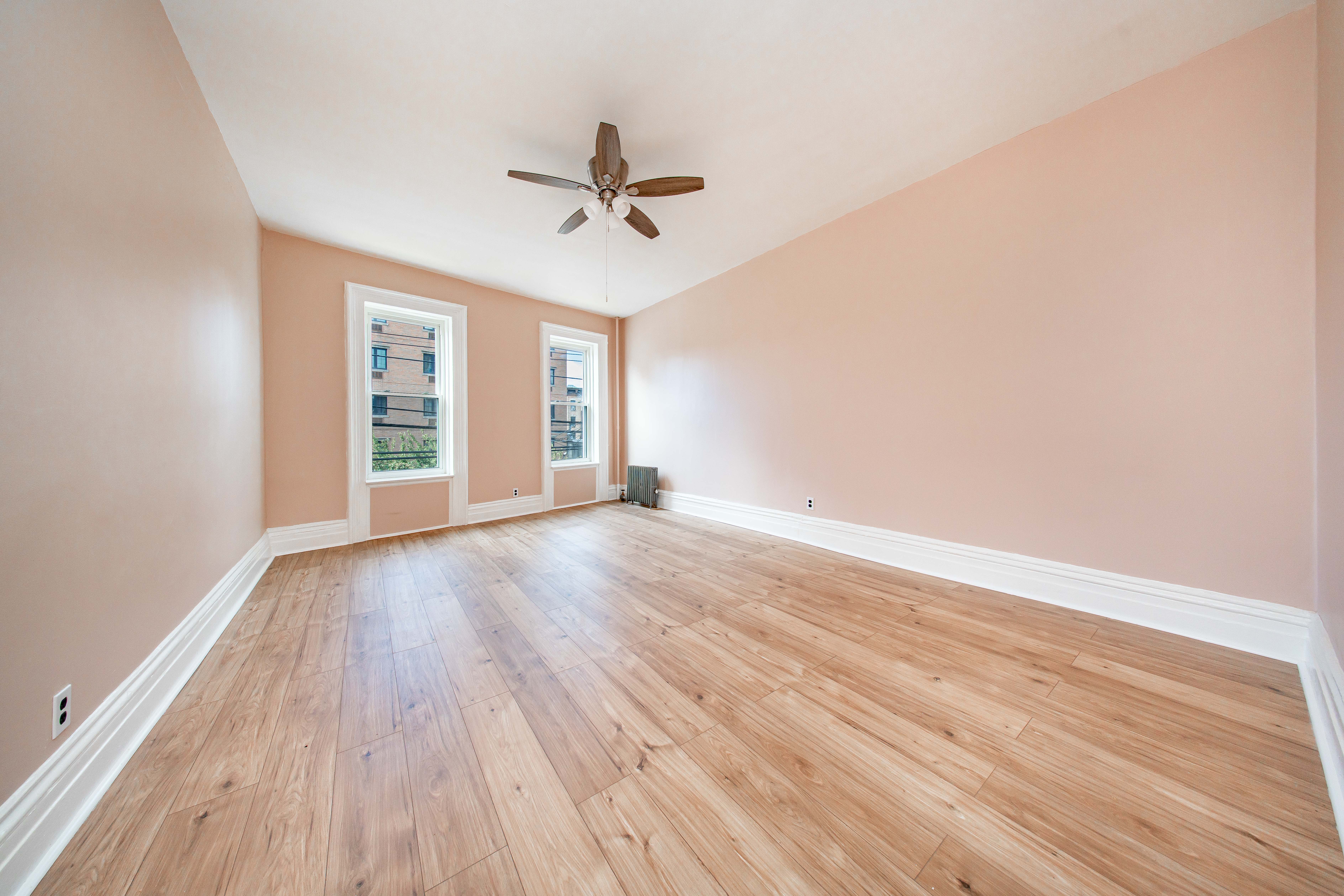 22-17 Astoria Boulevard, Unit 2W Queens, NY 11102 - Photo 1 of 10 an empty room with wooden floor fan and windows