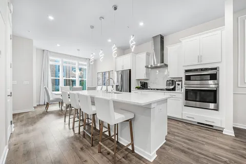 a kitchen with stainless steel appliances kitchen island granite countertop a stove top oven a sink a refrigerator with white cabinets and wooden floor
