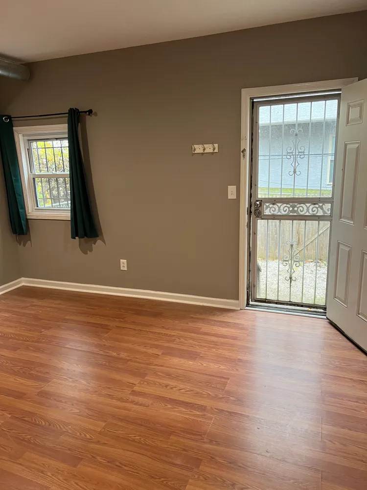 a view of an empty room with wooden floor and a window