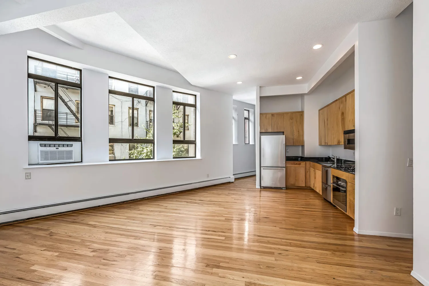 a view of an empty room with a window and wooden floor