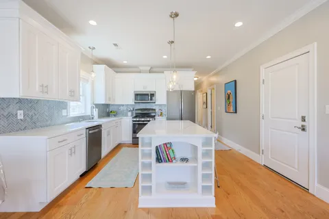 a white kitchen with wooden floor and stainless steel appliances