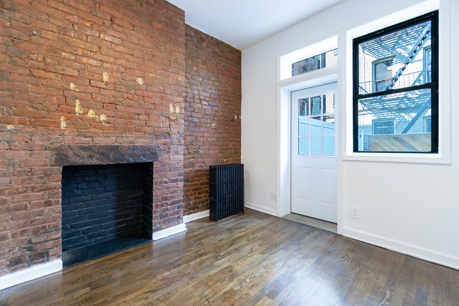 339 East 6th Street, Unit B Manhattan, NY 10003 - Photo 6 of 22 an empty room with wooden floor fireplace and windows