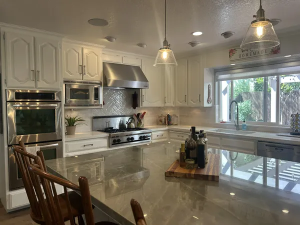 a kitchen with stainless steel appliances granite countertop a stove a refrigerator a sink a stove and white cabinets with wooden floor