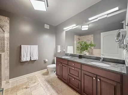 a spacious bathroom with a granite countertop double vanity sink a mirror and a toilet